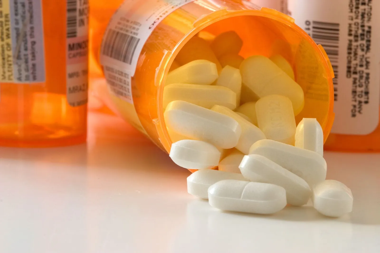 Does Hydrocodone Have Codeine In It? Three orange prescription pill bottles, one open on its side with white pills spilling out.