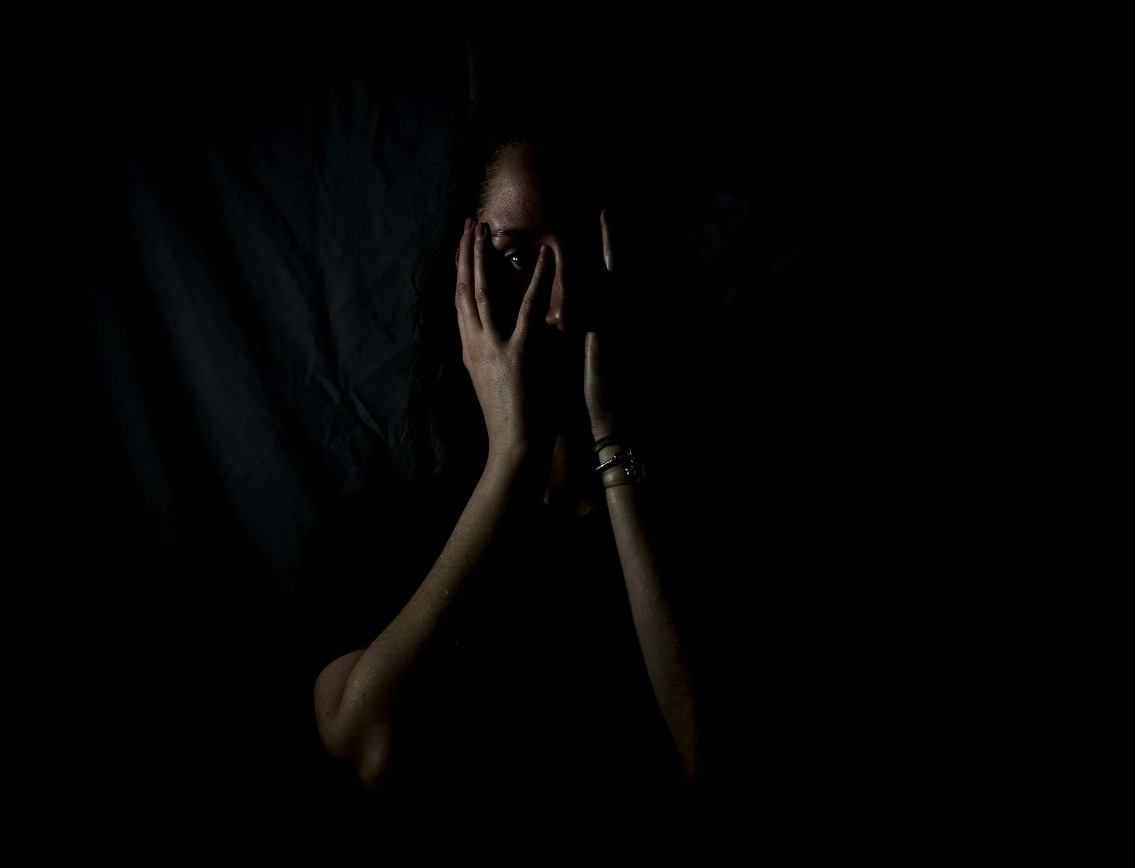 How Long Does PCP Stay In The System? A person standing in the dark with their hands to their face.