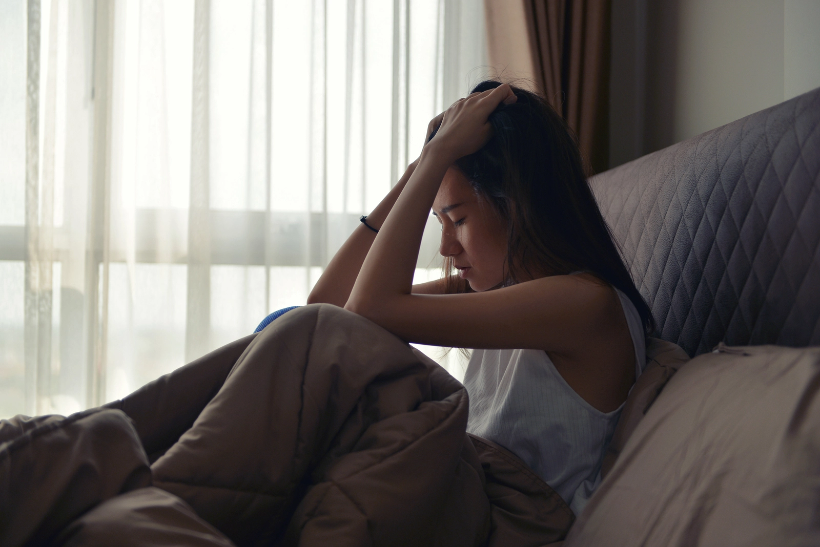 How Quickly Does Ambien Work? A woman sitting up in bed with her hands to her head.